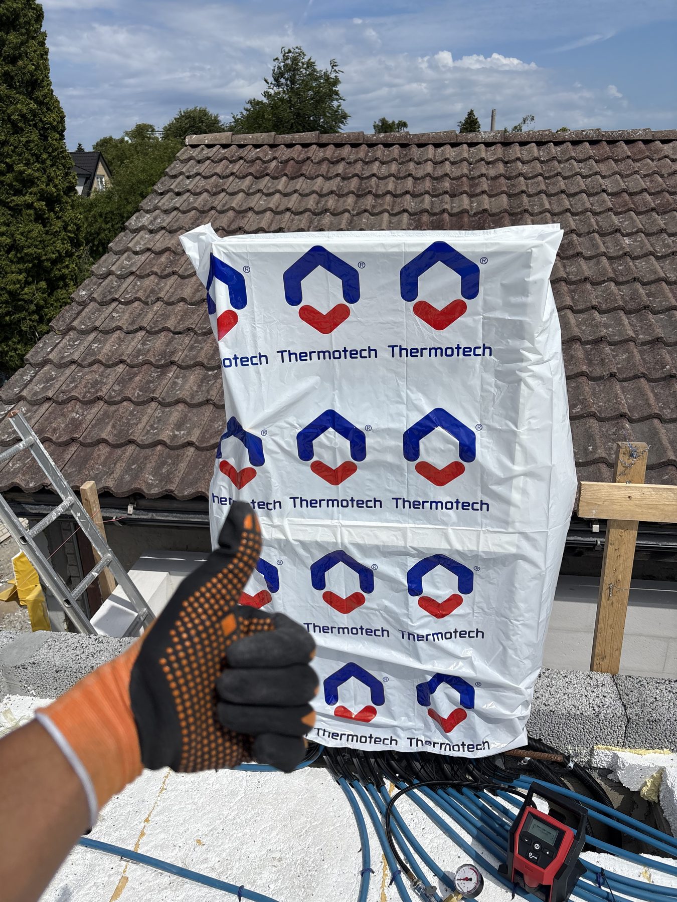 Montör ger tummen upp framför en förpackning med Thermotech golvvärmerör på ett tak