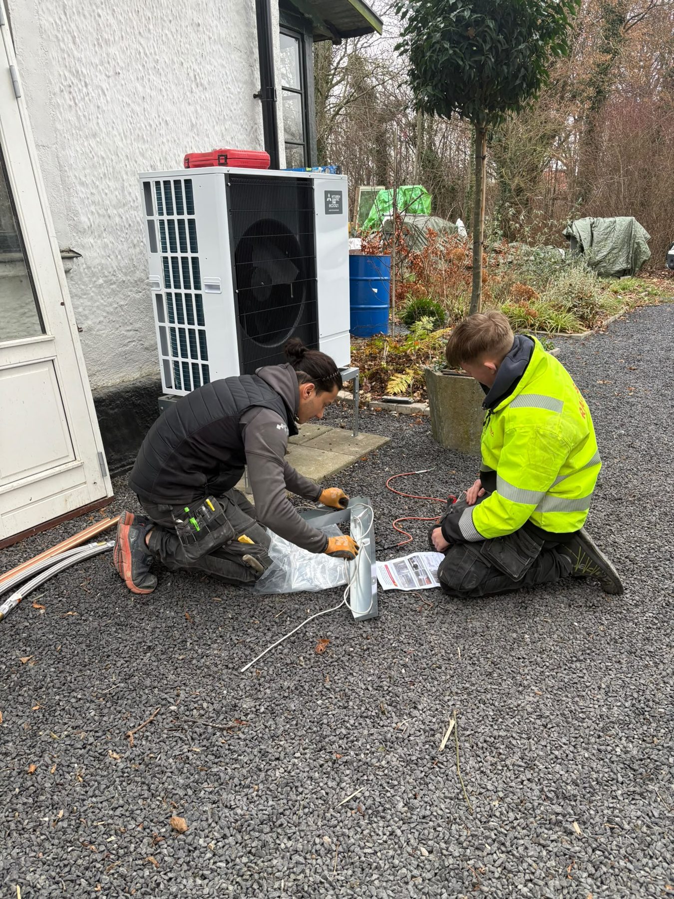 Två montörer från MJ VVS & Bygg installerar utomhusdelen till en värmepump vid en vit villa i Lund
